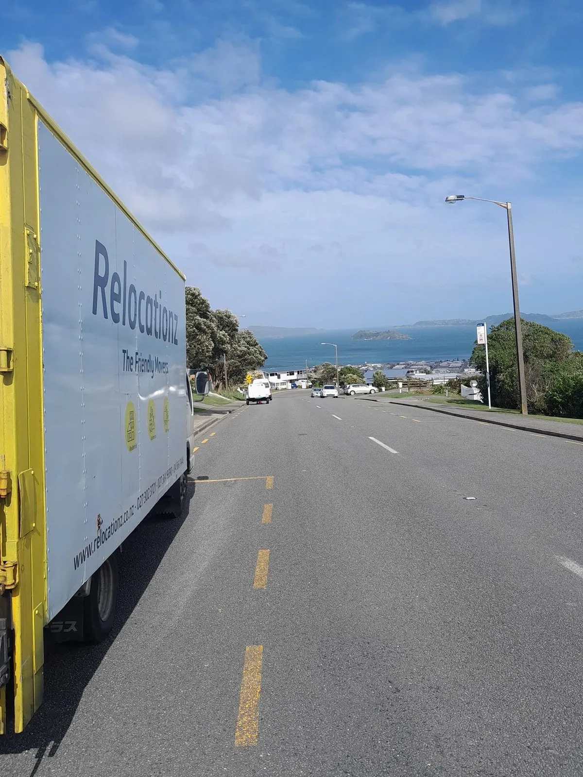 RelocatioNZ truck on a coastal road with the harbour in the distance